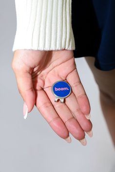 a woman's hand holding a blue badge with the word boom on it in front of her