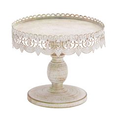 a white cake stand with an ornate design on the top and bottom, sitting on a table