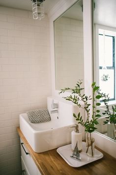 a white sink sitting under a bathroom mirror next to a wooden counter with a plant in it