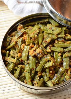 cooked green beans in a metal bowl on a bamboo mat next to a silver pan