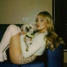 a woman sitting on a blue couch holding a small dog in her lap and posing for the camera