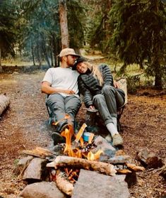 a man and woman sitting next to each other near a campfire in the woods