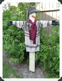 a wooden scarecrow standing in front of some bushes