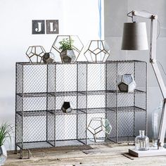 a metal shelf with plants in it on top of a wooden table next to a lamp