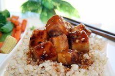 a white plate topped with tofu and rice covered in sauce next to carrots