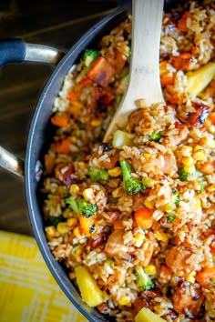 a pot filled with rice and vegetables on top of a yellow table cloth next to a wooden spoon