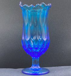 a blue glass vase sitting on top of a white tablecloth next to a gray wall