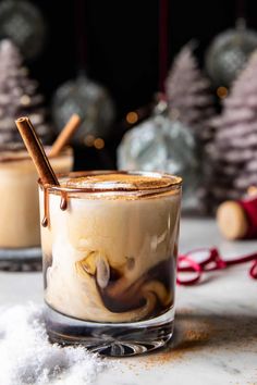 two glasses filled with hot chocolate and cinnamon sitting on a table next to christmas decorations