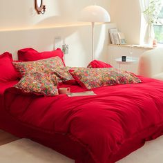 a bed with red sheets and pillows in a room next to a lamp on the wall