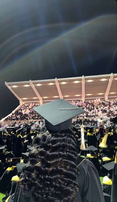 graduates in graduation gowns and caps are looking at the stage with bright lights behind them