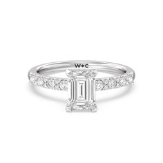 a white gold engagement ring with an emerald stone in the center and side stones on each band