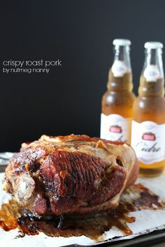 there is a large piece of meat on the table next to two bottles of beer