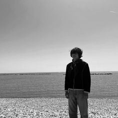 a man standing on top of a rocky beach next to the ocean with an airplane in the sky