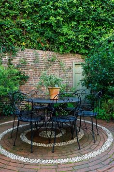 an outdoor table and chairs in the middle of a brick patio surrounded by greenery