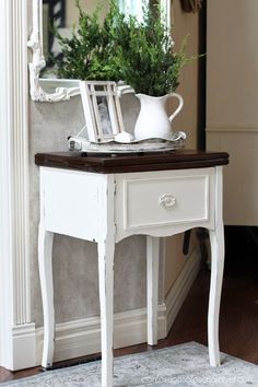 a small white table with a potted plant on top of it and a mirror behind it