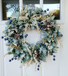 a wreath with blue berries, pine cones and greenery hangs on the front door