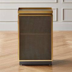 a gold and black speaker sitting on top of a hard wood floor next to a white wall