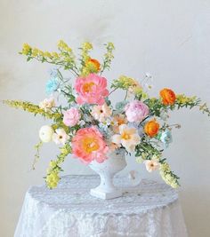 a white vase filled with lots of colorful flowers on top of a lace covered table