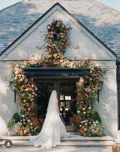 a bride standing in front of a white building with flowers on it's side