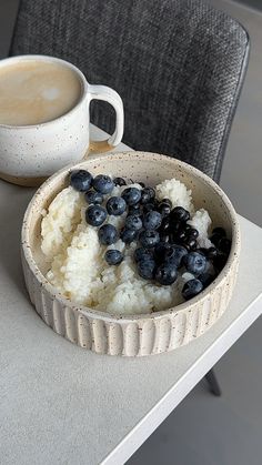 a bowl of rice and blueberries next to a cup of coffee on a table