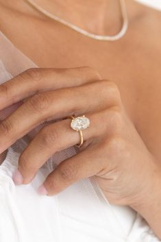 a close up of a person's hand with a ring on their finger, wearing a white dress