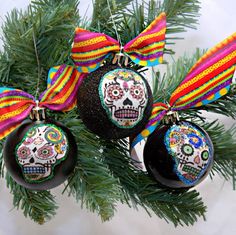 three ornaments hanging from a christmas tree decorated with colorful ribbons and sugar skull decorations on them