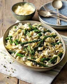 a bowl filled with pasta and asparagus on top of a table next to two plates