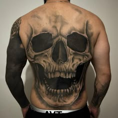 the back of a man with a skull tattoo on his upper and lower back,