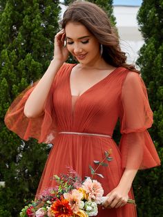 a woman in an orange dress is holding a bouquet and talking on her cell phone