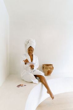 a woman sitting on top of a white table next to a vase