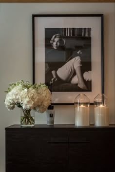 candles and flowers sit on a dresser in front of a framed black and white photograph