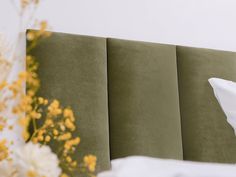 a green headboard with white pillows and yellow flowers in the corner next to it