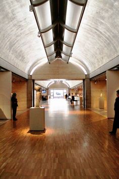 people are standing in an open space with wooden floors and walls, while one person is walking down the hall