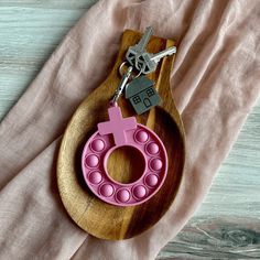 a wooden keychain with a pink pacifier and cross on it, sitting next to a pair of keys