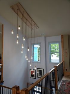 a staircase with lights hanging from the ceiling and pictures on the wall above it in front of a window