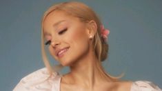 a woman with long blonde hair wearing a pink flower in her hair and smiling at the camera