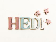 the word hedi spelled with wooden letters and flowers on a white wall behind it