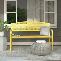 a yellow bench sitting in front of a window next to a vase and potted plant