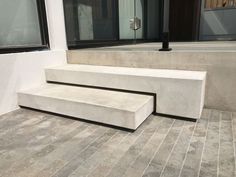 a concrete bench sitting in front of a window on the side of a building,