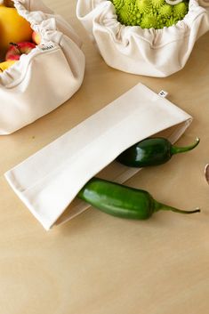 some green peppers are sitting on a table next to white bags with vegetables in them