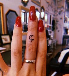 a woman's hand with a small crescent tattoo on her left ring, and a red manicure