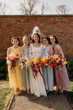 a group of women standing next to each other holding bouquets in front of a brick wall