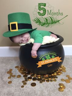 a baby in a green hat is laying on top of a pot of gold coins