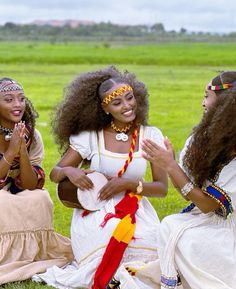 three women dressed in native american clothing sitting on the grass with their hands clasped together