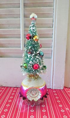 a small christmas tree sitting on top of a red and white table cloth next to a window