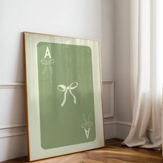 a framed poster with a bow on it in front of a white wall and wooden floor