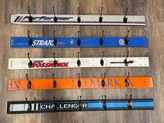 five skis are hanging from hooks on a wooden floor with the names of different skiers