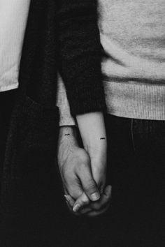 two people holding hands with tattoos on their arms