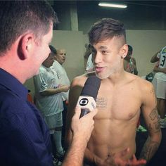 a man with no shirt on talking to someone in front of other people and holding a microphone