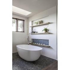 a large white bath tub sitting in a bathroom next to a window with open shelves